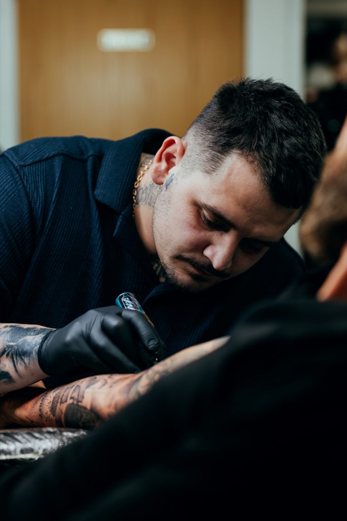 Tätowierer von Imperial Tattoo sticht konzentriert ein Motiv auf einen Unterarm
