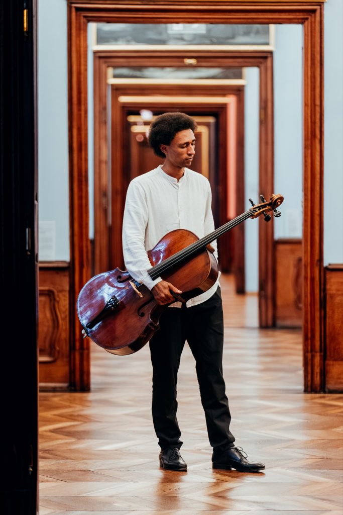 Cellist trägt sein Instrument durch die Türflucht des Palais